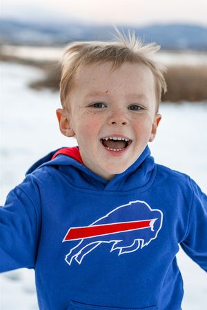 Young fan wearing a bright blue Buffalo Bills NFL team hoodie smiles in a snowy winter setting.