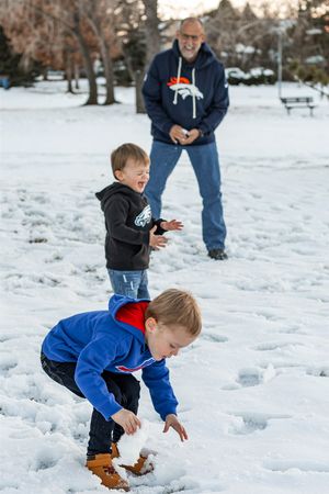 Kids playing and exploring in a snowy winter landscape with trees and benches in the background.