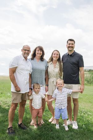 Multi-generational family poses together outdoors on grassy hill with cloudy sky.