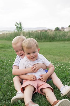 Two young children cuddling and laughing together in a grassy meadow with wildflowers.
