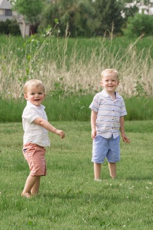 Two young children in casual summer clothes play and smile in a grassy field.