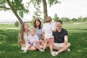 Extended family gathering on grass under trees on a bright summer day.