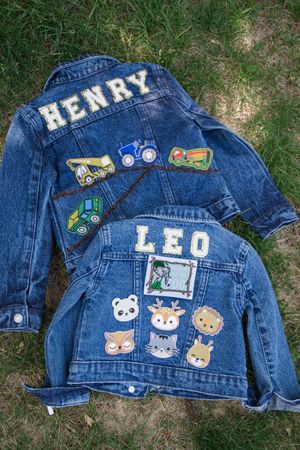 Denim jackets laid on grass displaying cute animal patches and personalized names.