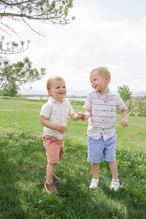 Two young children in summer outfits laughing together on grassy hillside.