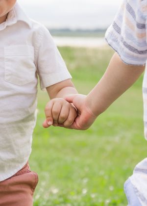 Close-up of two children's hands clasped together while standing outside.