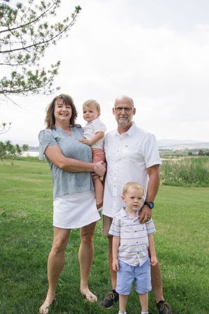 Family of four poses together on grassy hill with cloudy sky in background.