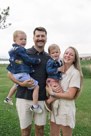 A family of four dressed in casual attire smiles together on a grassy hillside.
