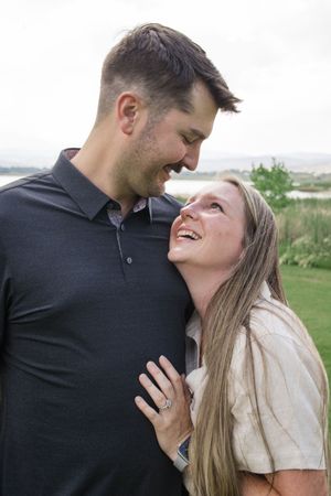 A couple shares an intimate moment laughing together on a grassy hillside.