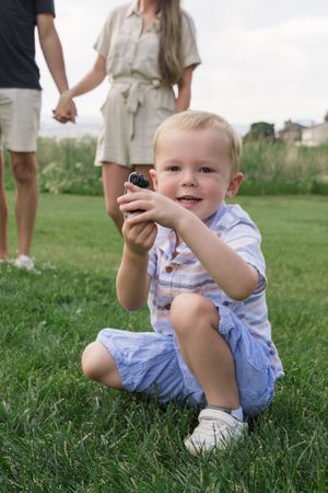 A child in blue and white striped clothing crouches on grass while holding something.