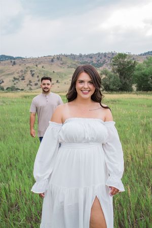 A couple in coordinated outfits standing in a grassy meadow with rolling hills behind them.