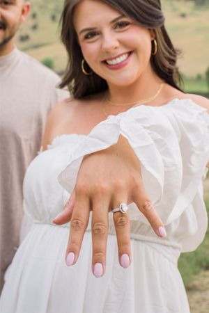 A close-up shot showing an engagement ring on a hand with mountains in the background.