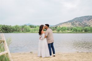 A romantic couple embracing by a lake with mountains in the background.