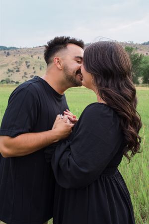Couple sharing intimate moment in black outfits against backdrop of mountain landscape.