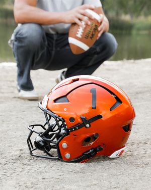 Three orange football helmets placed on the ground with black face masks and modern protective designs.