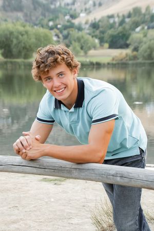 Person in light blue polo shirt lying on wooden dock by a lake with mountains in background.