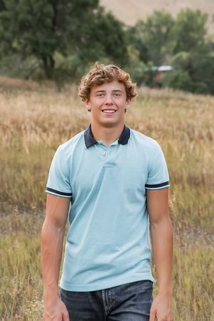 A casual portrait session in a golden field shows someone wearing a light blue collared shirt against nature.