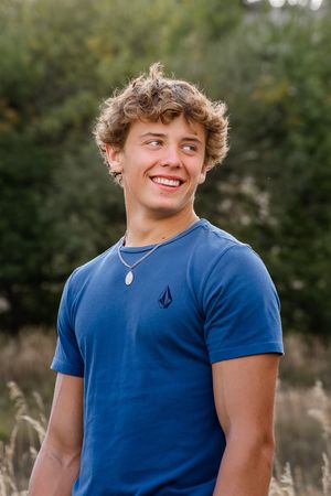 Casual portrait shot of someone in a blue t-shirt against a natural outdoor background.