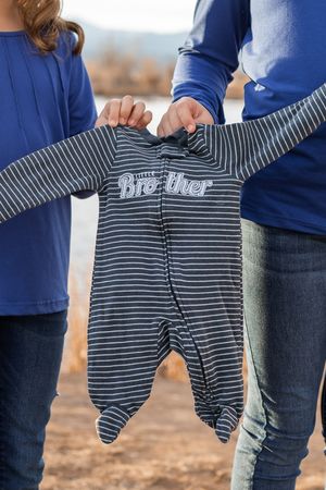 A striped baby onesie is held up between two people wearing blue tops and jeans.