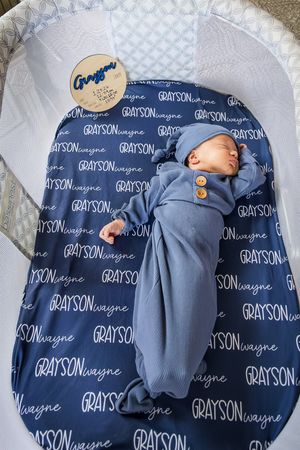 A newborn baby sleeping on a navy blue personalized name blanket with repeating text pattern.