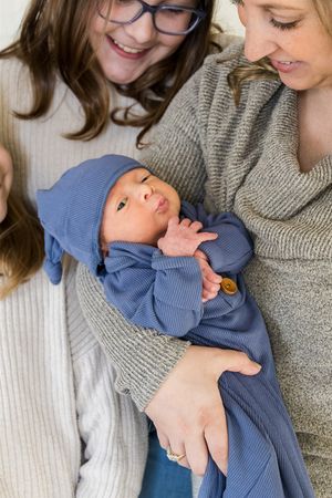 A baby in blue sleepwear rests peacefully in someone's arms while wearing a cozy knit outfit.