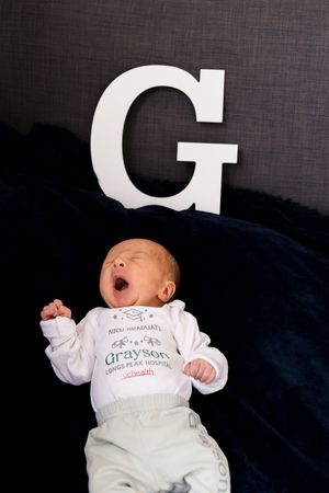 A baby in white clothing lies on dark bedding with large white letter decorations visible.
