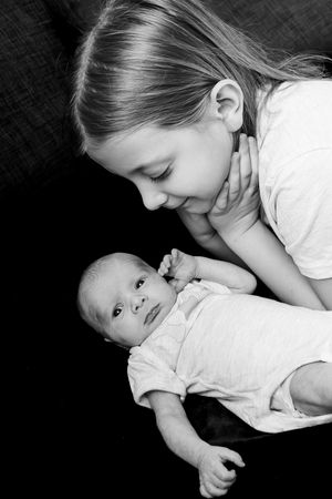 A series of black and white photos showing tender moments between a baby and child in white clothing.