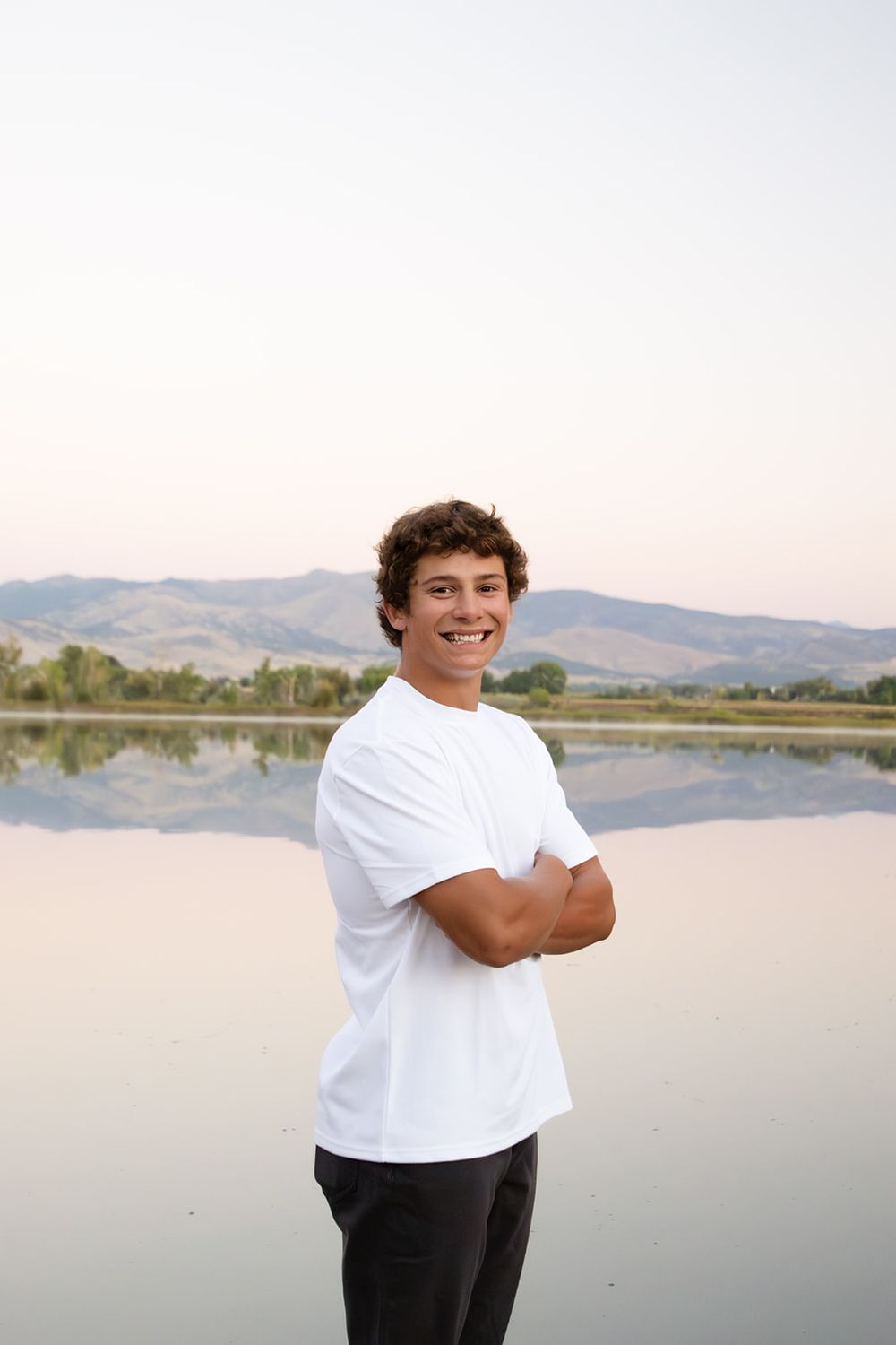 Senior portrait session near a serene lake with mountains in the background.