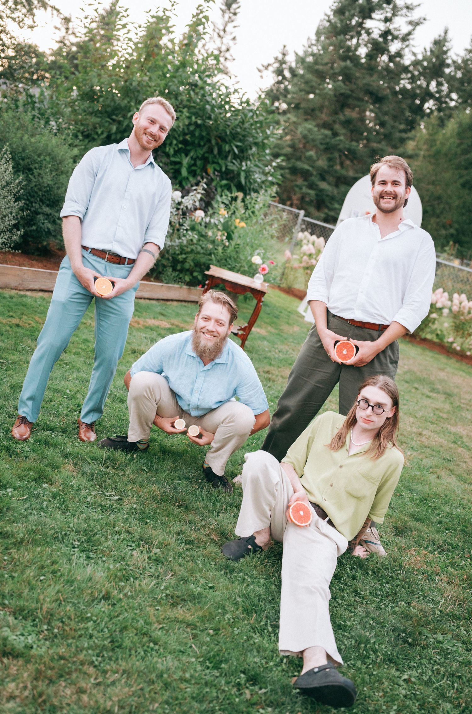 A group of four people in casual attire posing on a grassy lawn with trees in the background.
