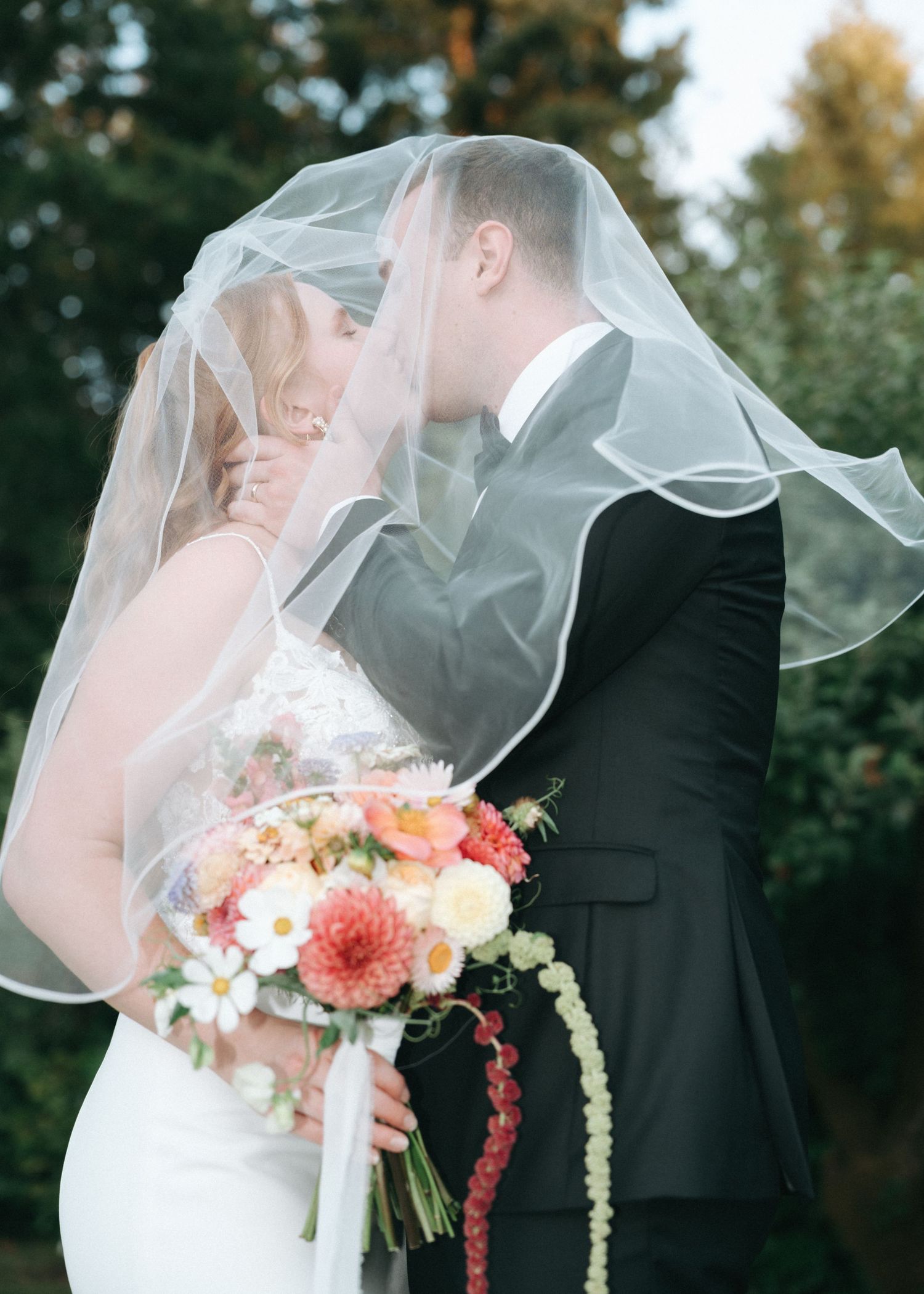 Wedding couple shares intimate moments in outdoor garden setting with coral and peach floral bouquets.