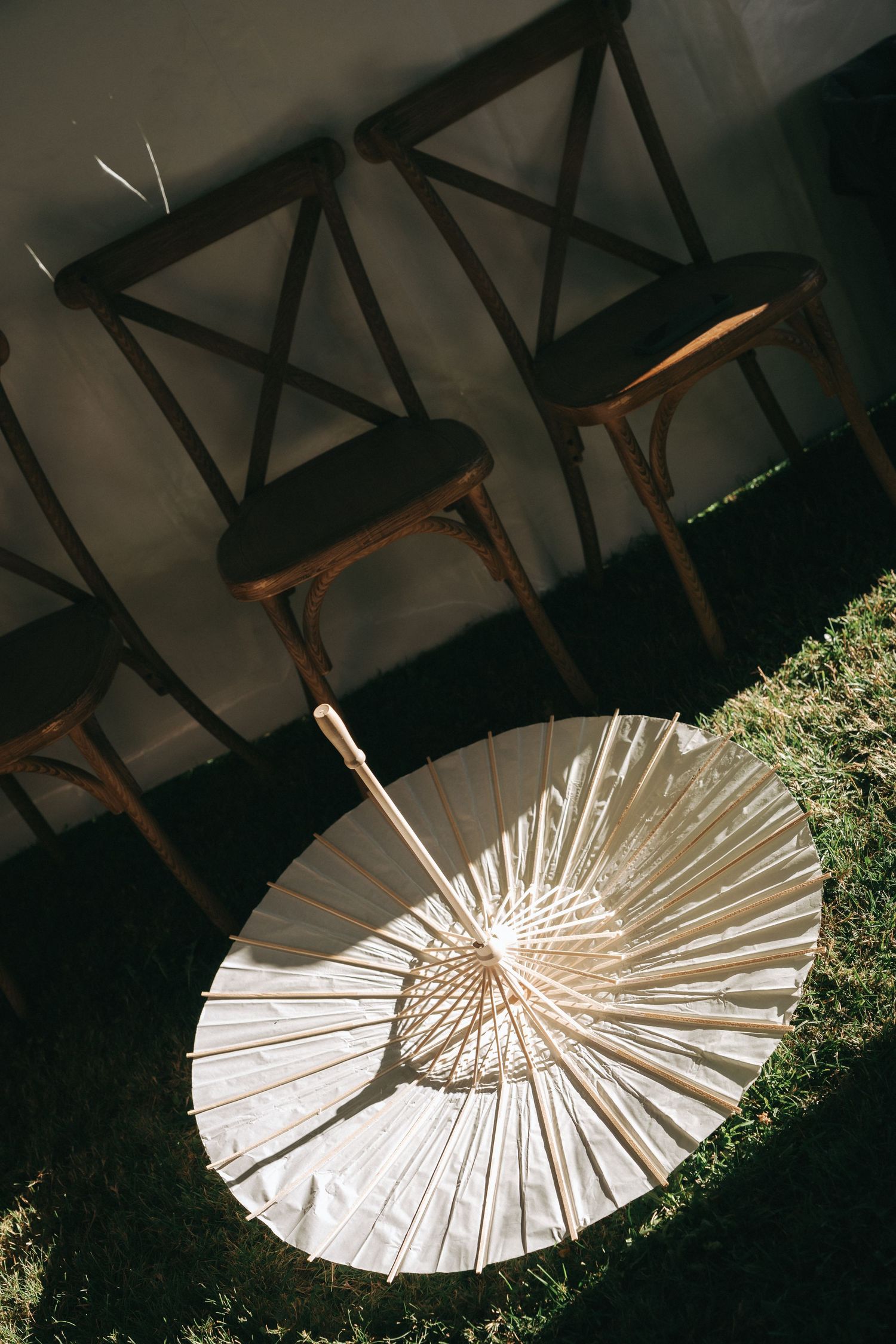 A white decorative paper parasol umbrella rests on grass beneath wooden chairs and beams.