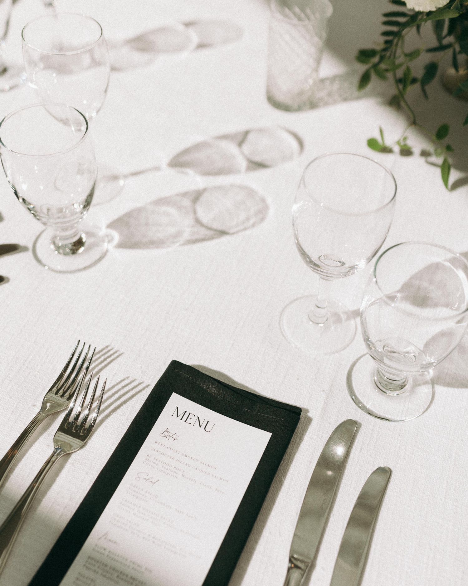Elegant white table setting with menu card, silverware, and wine glasses.