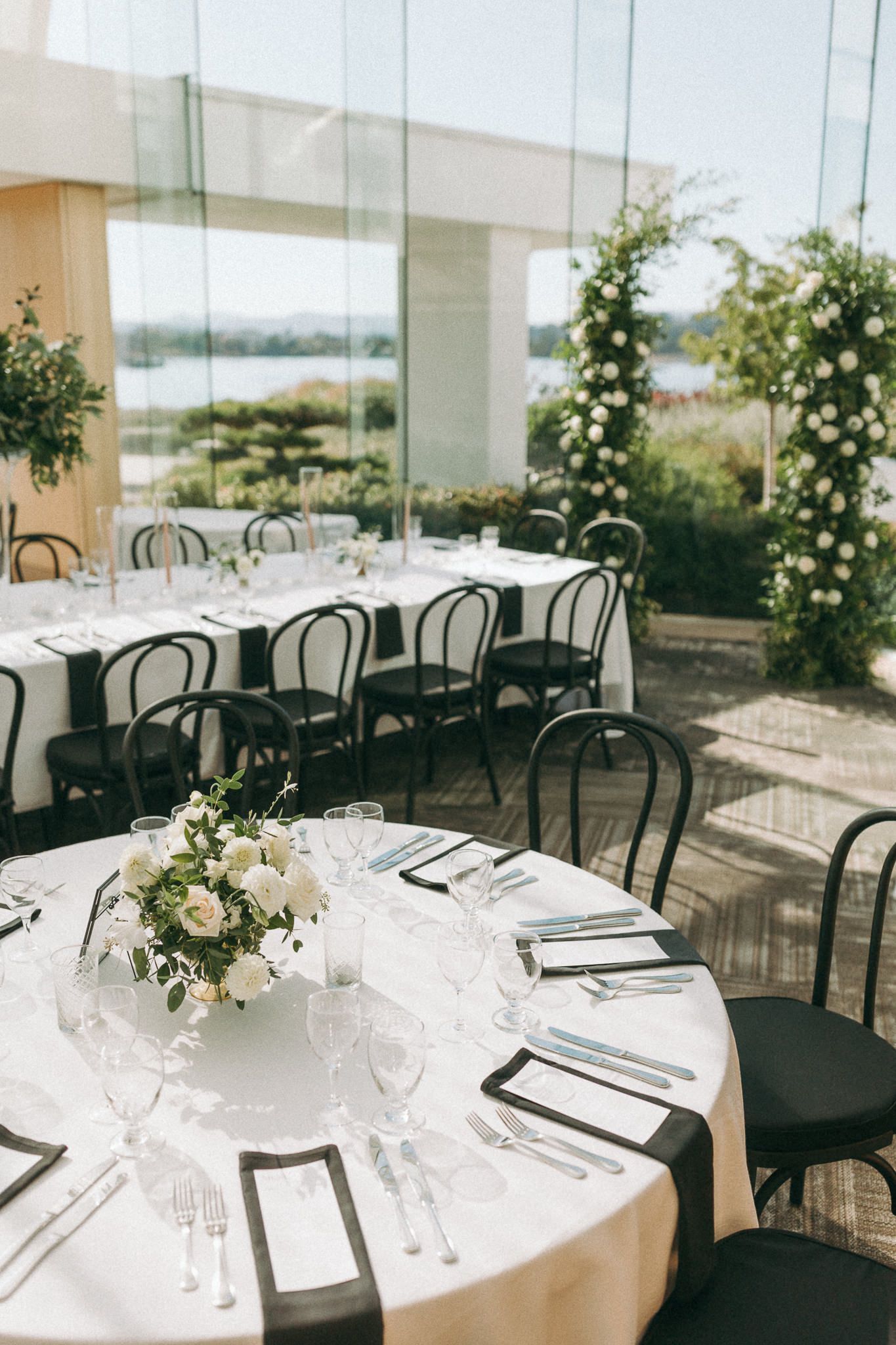 Modern wedding reception venue with round tables and glass walls overlooking water.