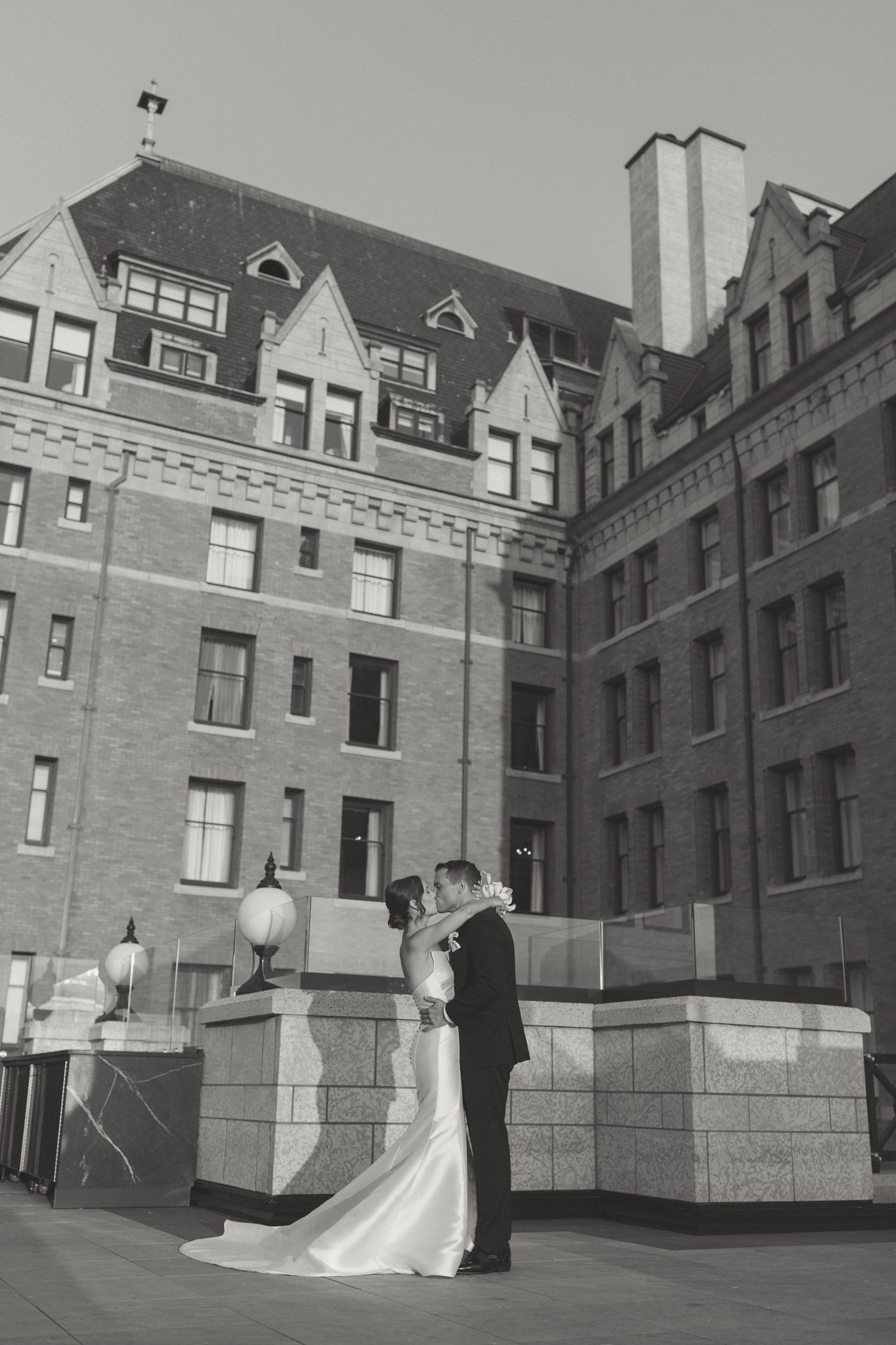A wedding couple embracing on a rooftop terrace with historic brick architecture in the background.