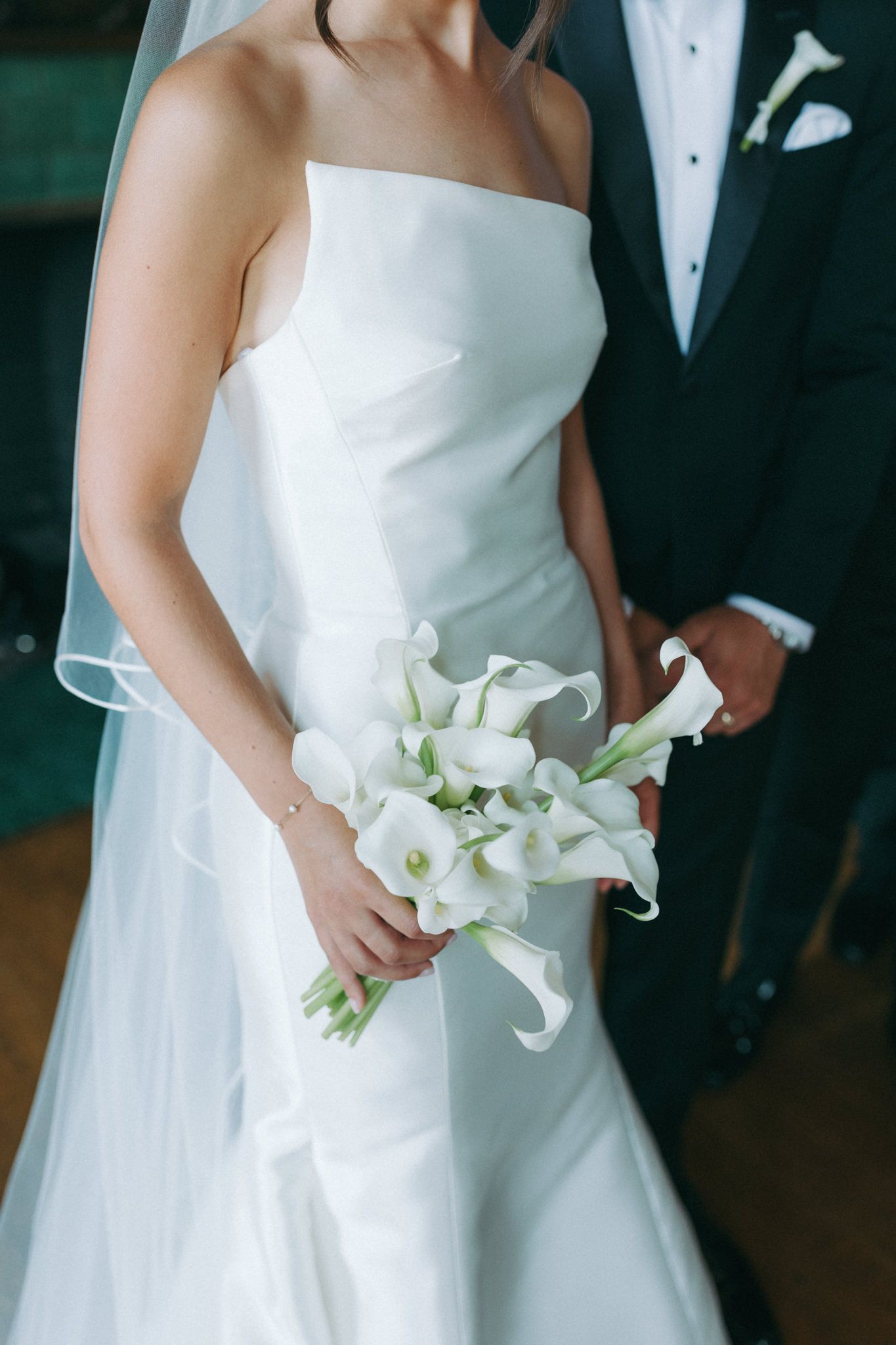 Classic white wedding dress with calla lily bouquet against dark background.