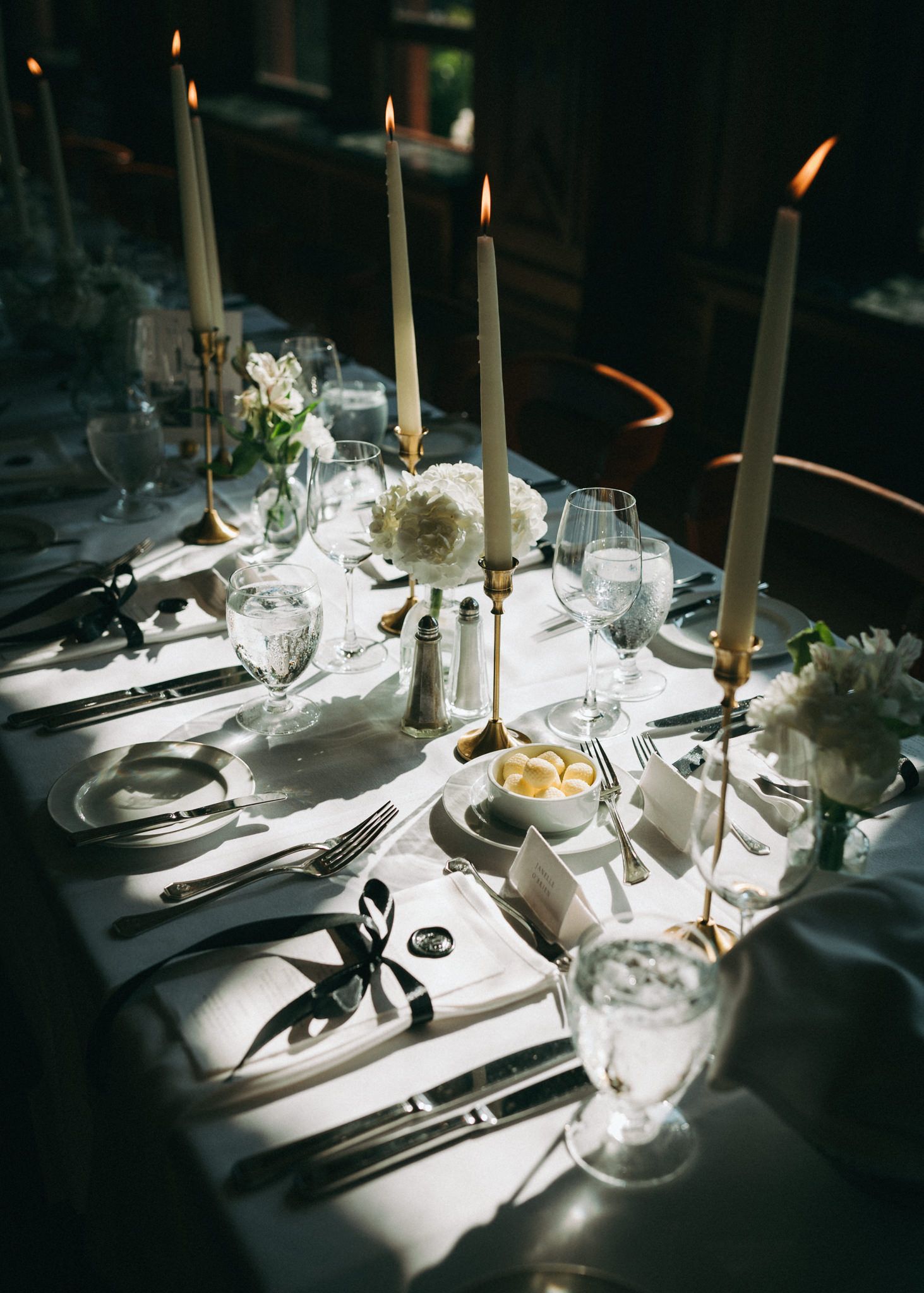 Elegant table setting with white linens and tall candles casting dramatic shadows.