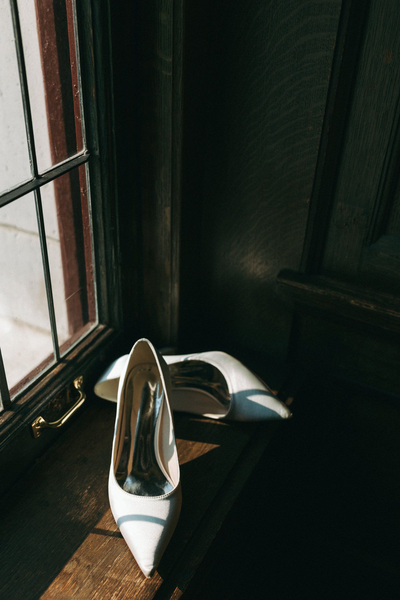 White bridal shoes sit in dramatic window lighting creating elegant shadows.