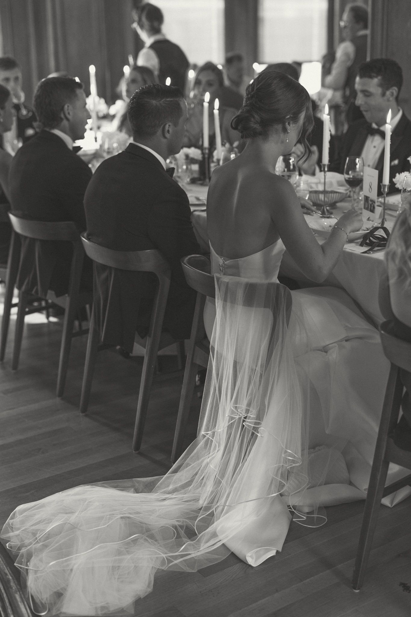 A wedding reception scene with guests dining and a bride in a flowing white gown.