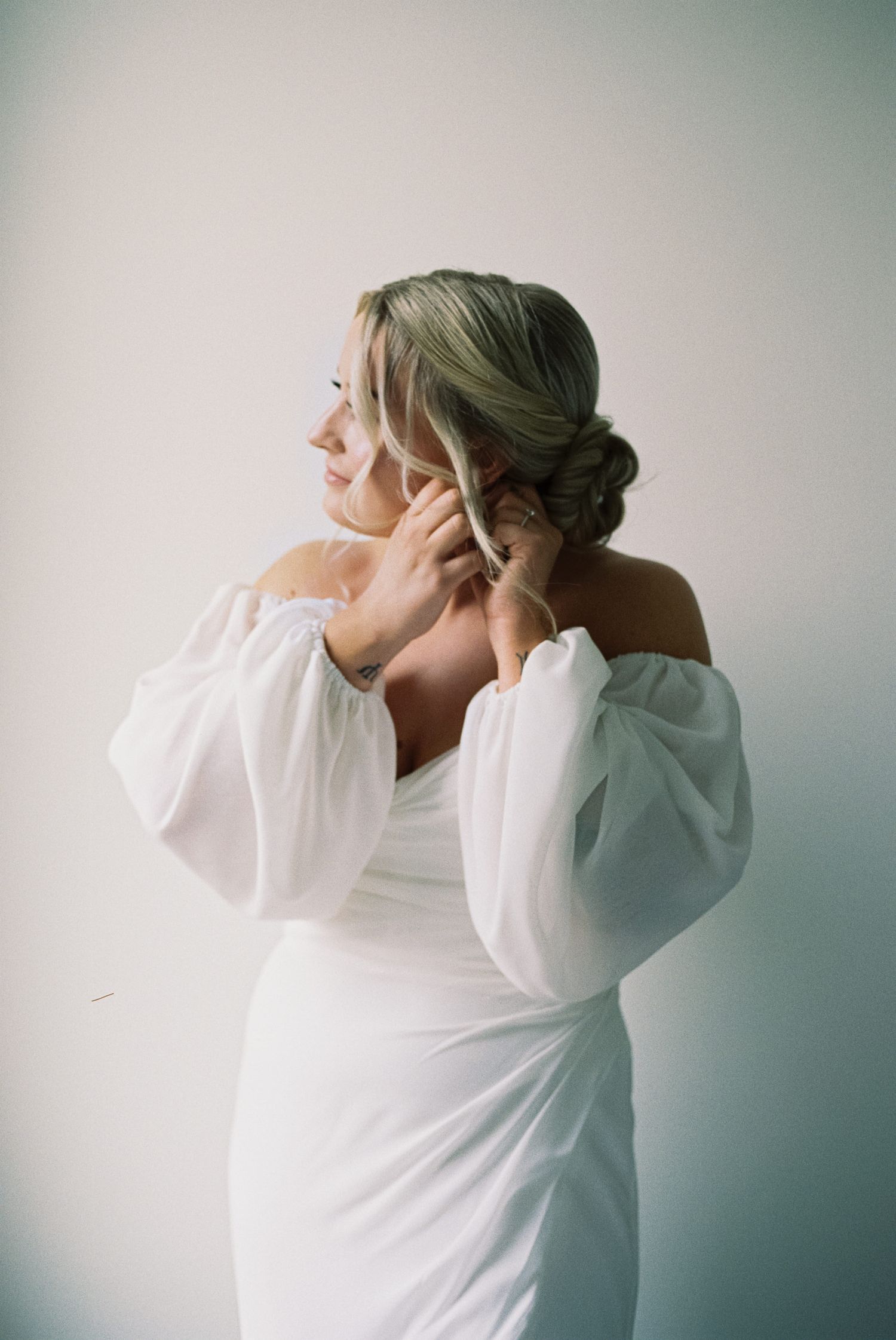 Film photography image of a bride turned to the side and putting on her earrings.