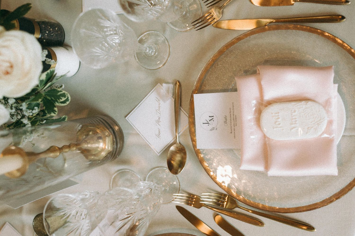 Luxurious wedding table setting with gold cutlery and crystal glassware against a white tablecloth.