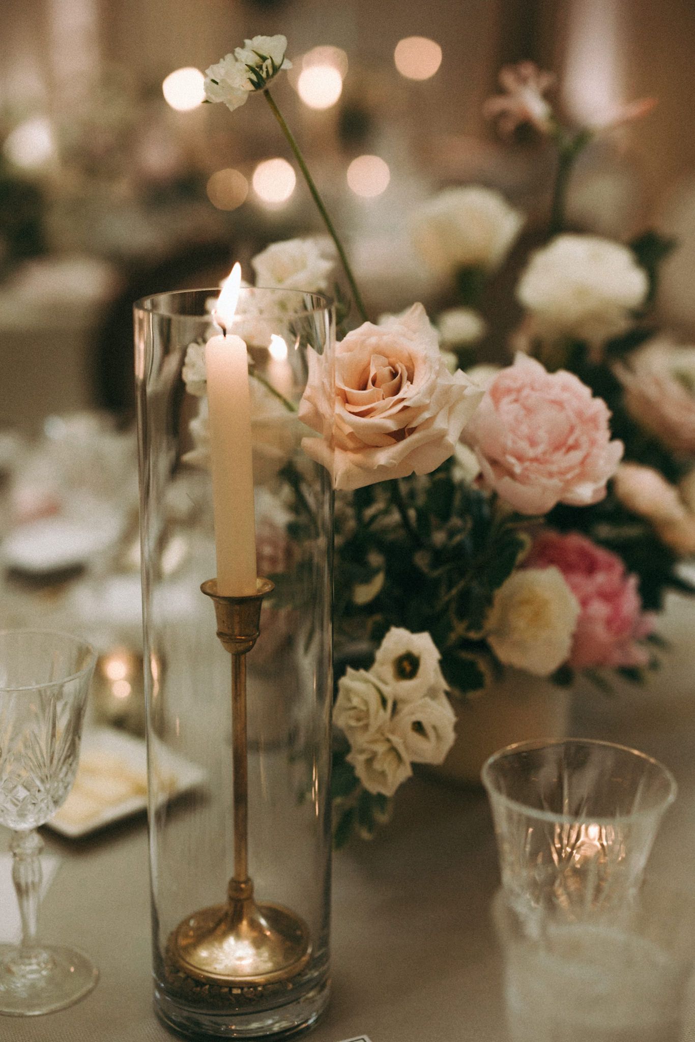 Romantic wedding reception centerpiece with blush roses and glowing candles creating intimate ambiance.