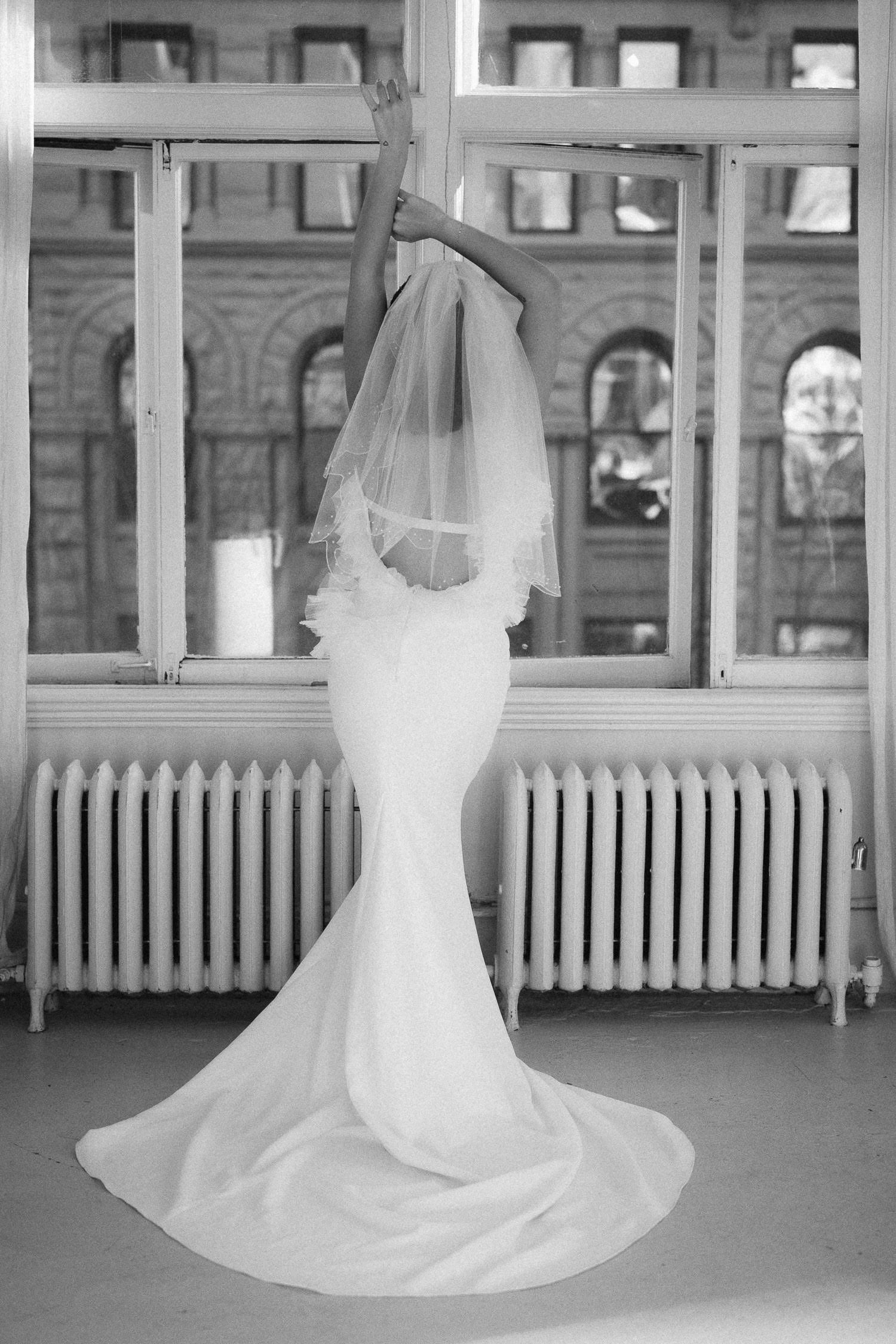 Multiple white wedding dresses displayed in a room with large windows and radiators.
