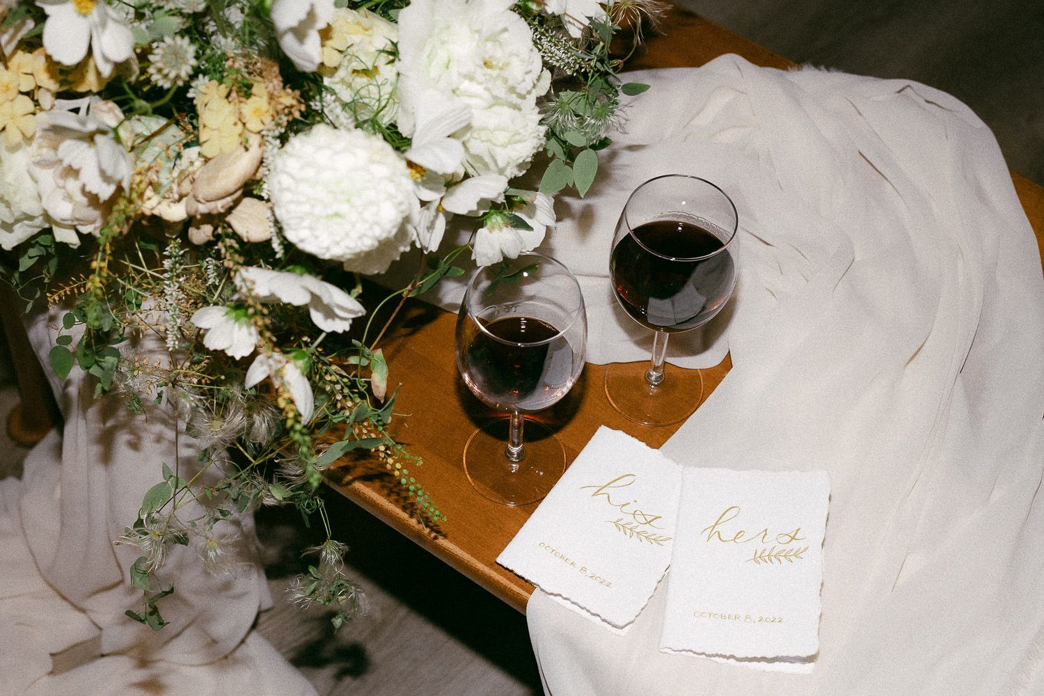 Elegant white floral arrangements and wine glasses set on a wooden table at a wedding reception.