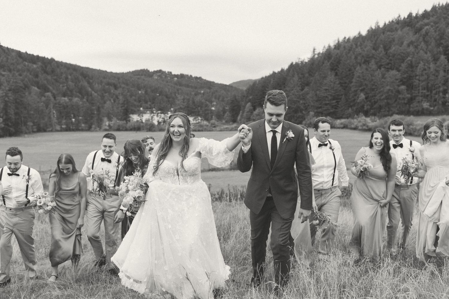 Wedding party walking through a meadow with mountains in the background.