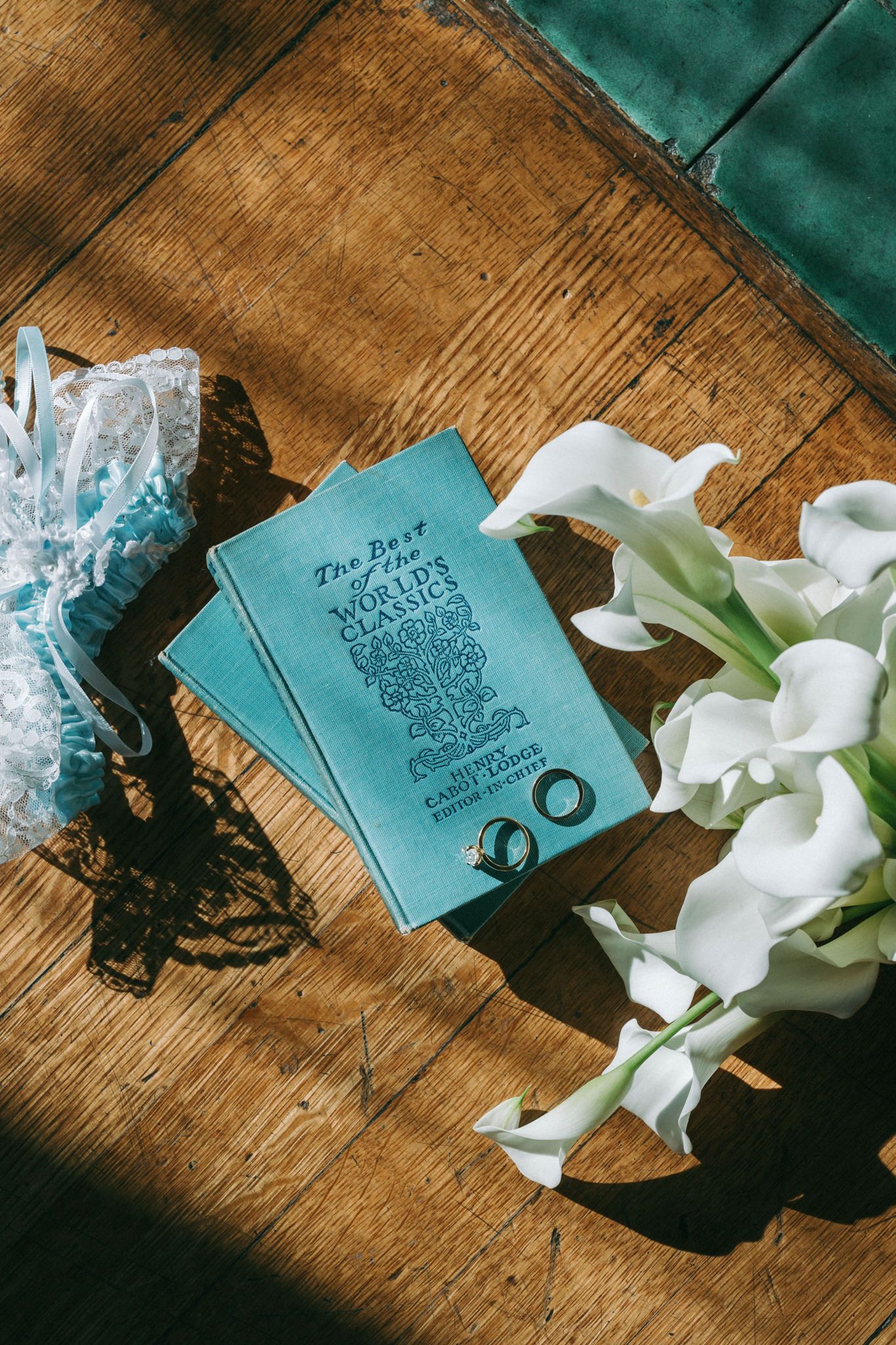 A teal wedding program book with white calla lilies on wooden surface.
