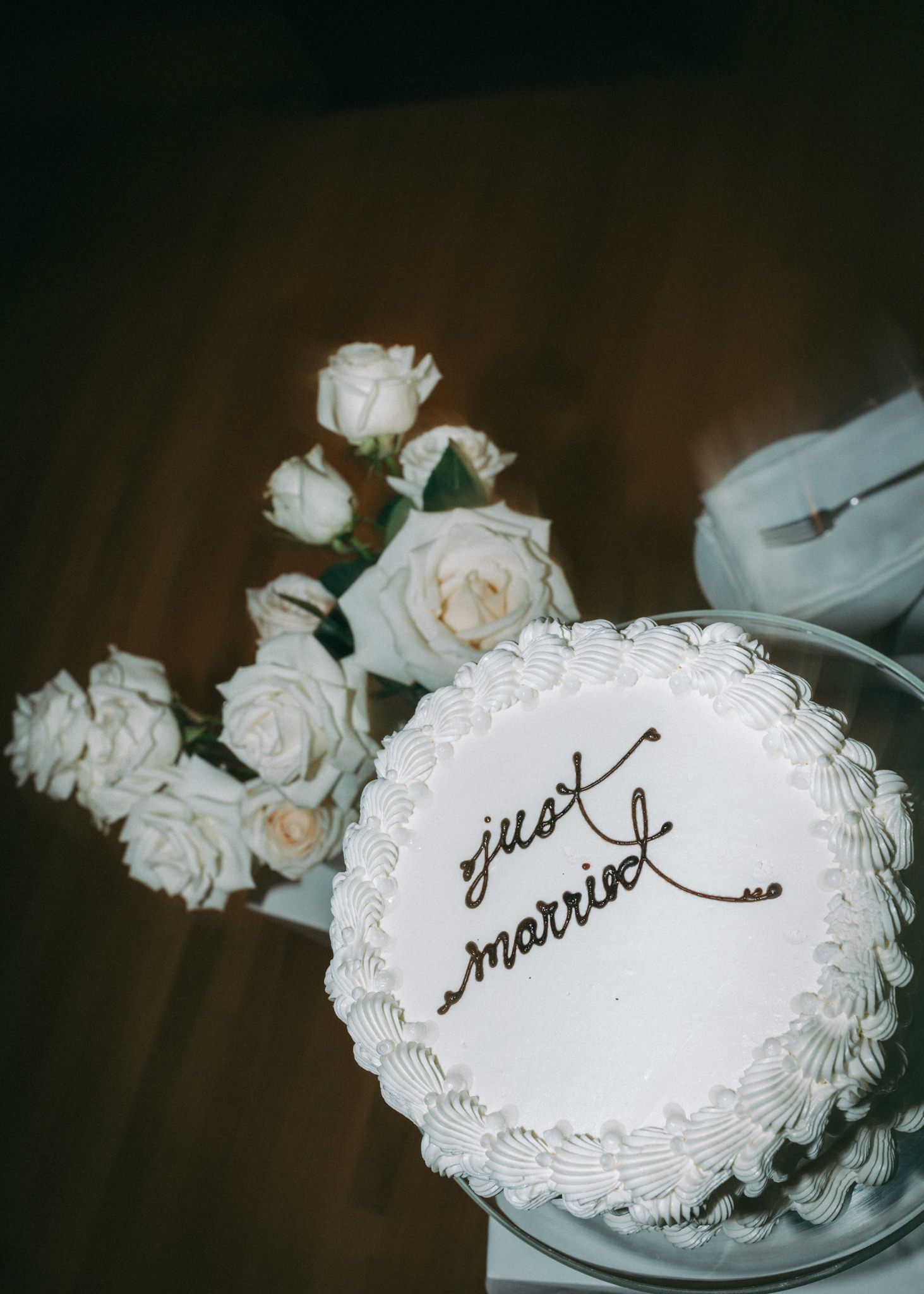 A white wedding cake decorated with roses and 'just married' text written in cursive.