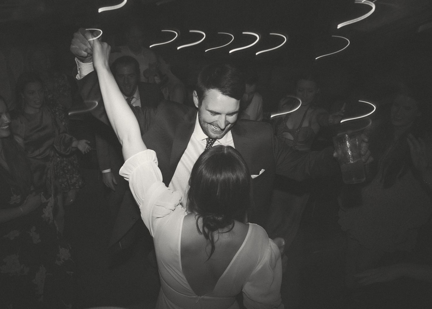 Black and white photo of people dancing at a wedding reception with light trails above.