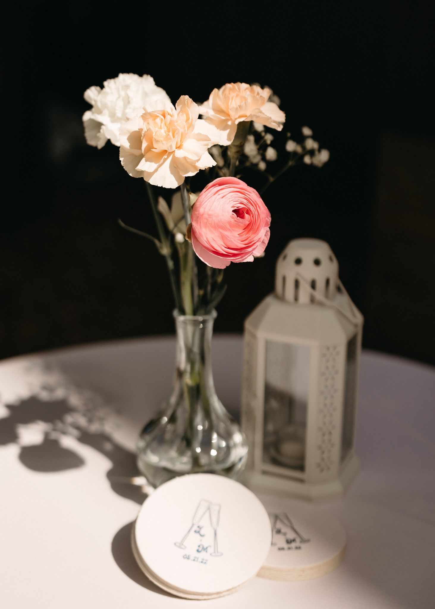 Elegant floral centerpieces with pink ranunculus and white flowers in glass vases alongside decorative lanterns.
