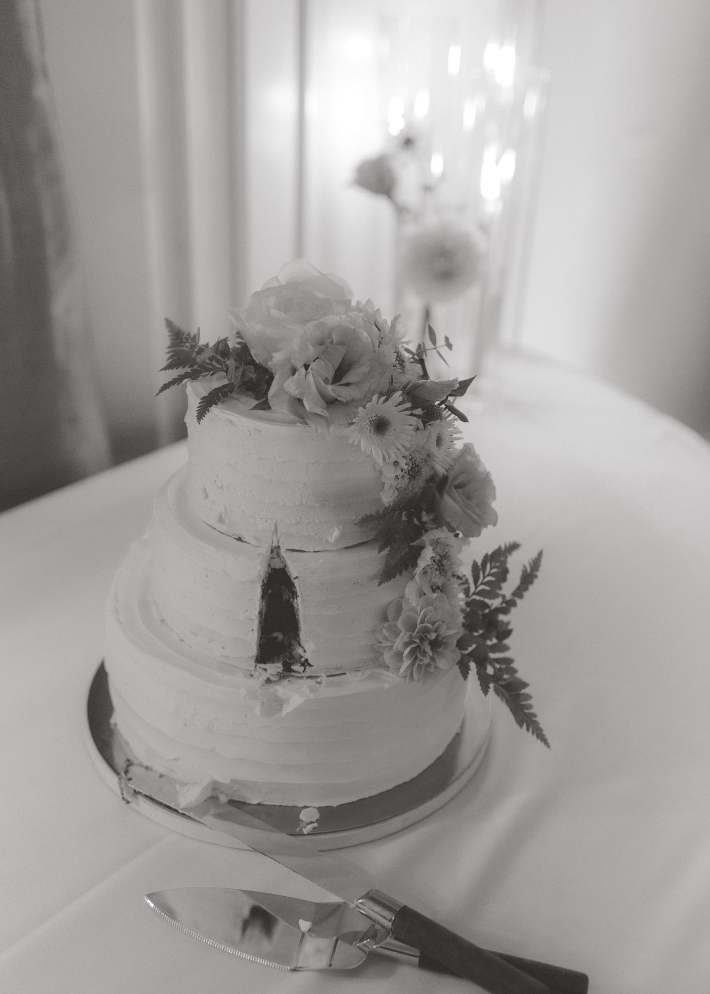 White wedding cake decorated with delicate flowers and greenery on a white tablecloth.