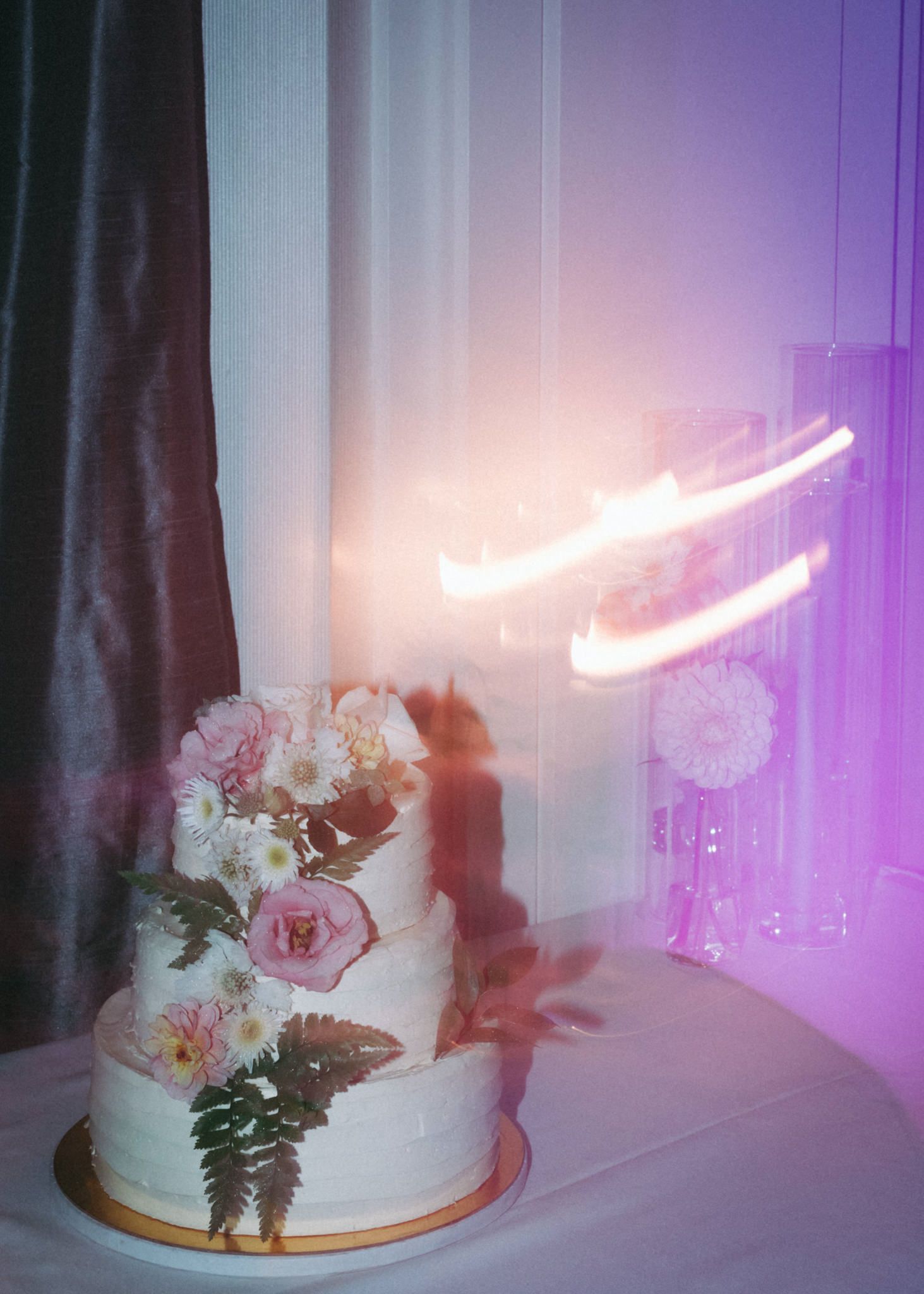 Wedding cake display with neon light and floral decorations in purple ambient lighting.