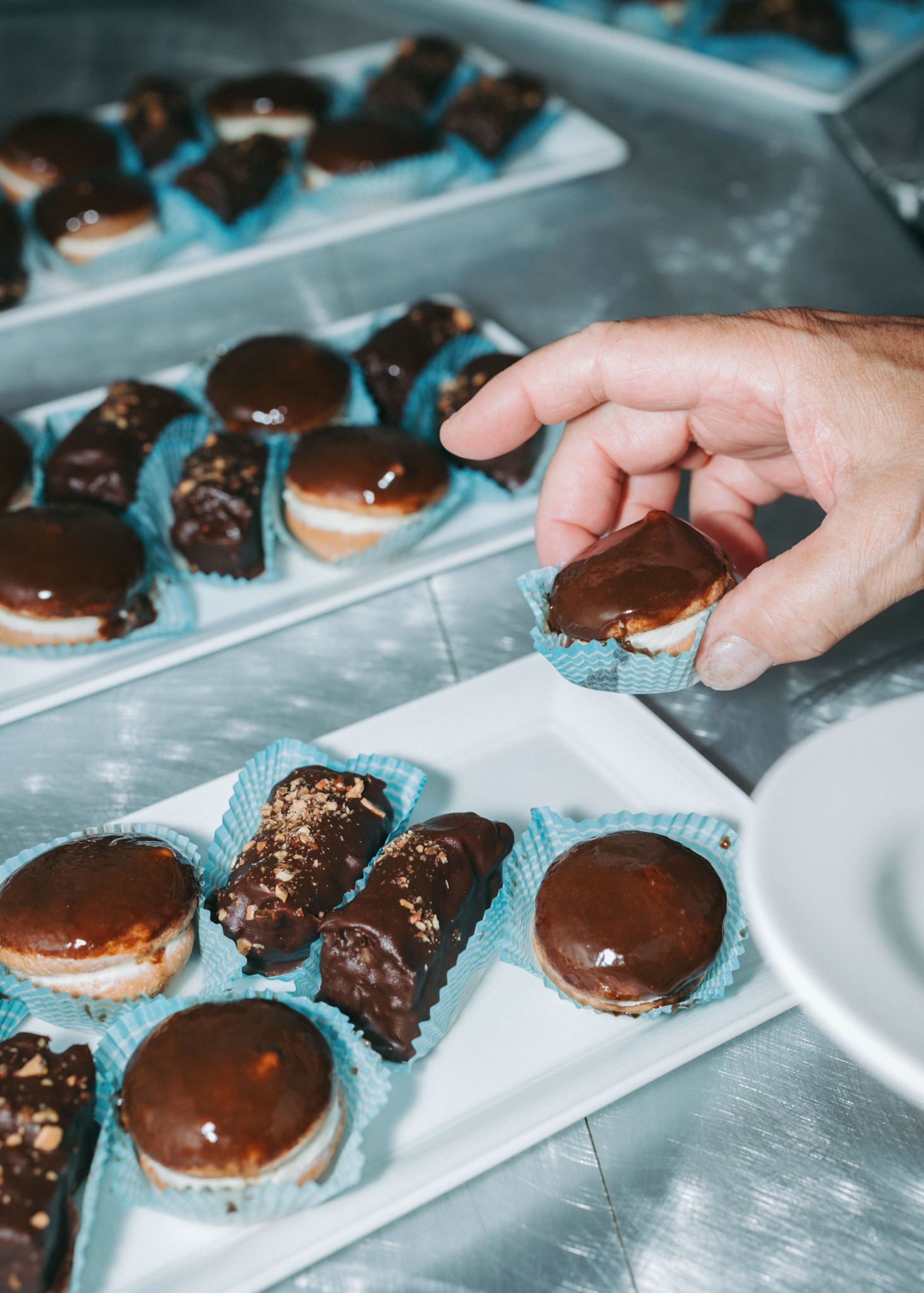 Chocolate-covered desserts arranged on serving trays with hands reaching to arrange them.